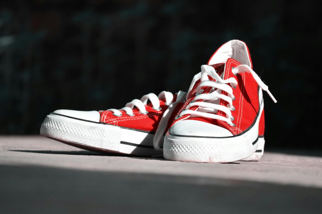 Close-up of vibrant red canvas sneakers with white laces on an outdoor surface.