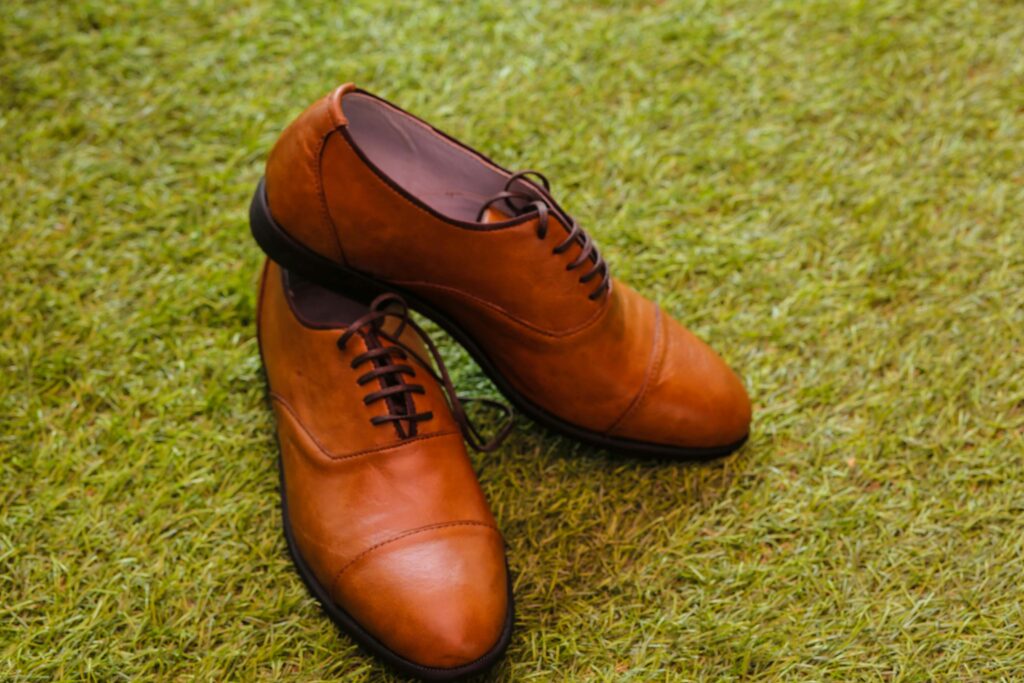 Pair of elegant brown leather shoes resting on fresh green grass, outdoor setting.