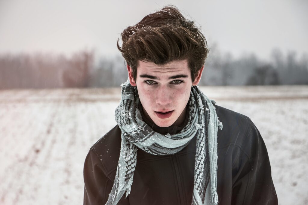 Portrait of a young man outdoors in a snowy field wearing a scarf.